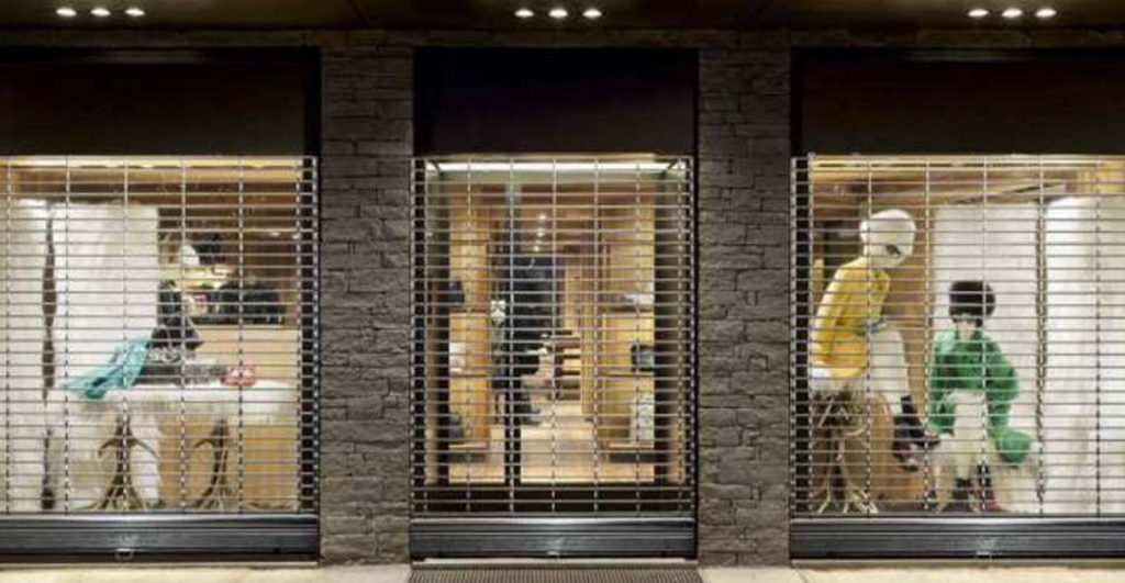 Portail métallique gris anthracite installé devant la devanture vitrée d’un magasin en centre-ville, assurant sécurité et protection de l’entrée.