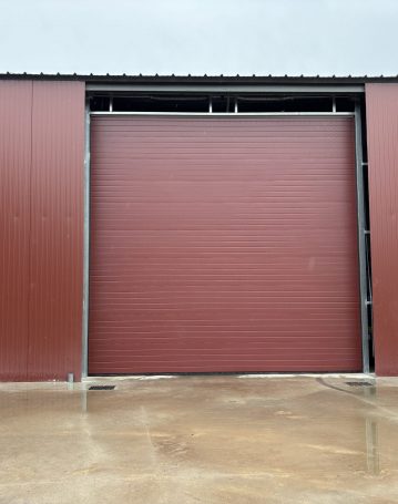 Hangar agricole rouge avec grande porte sectionnelle isolée en façade.